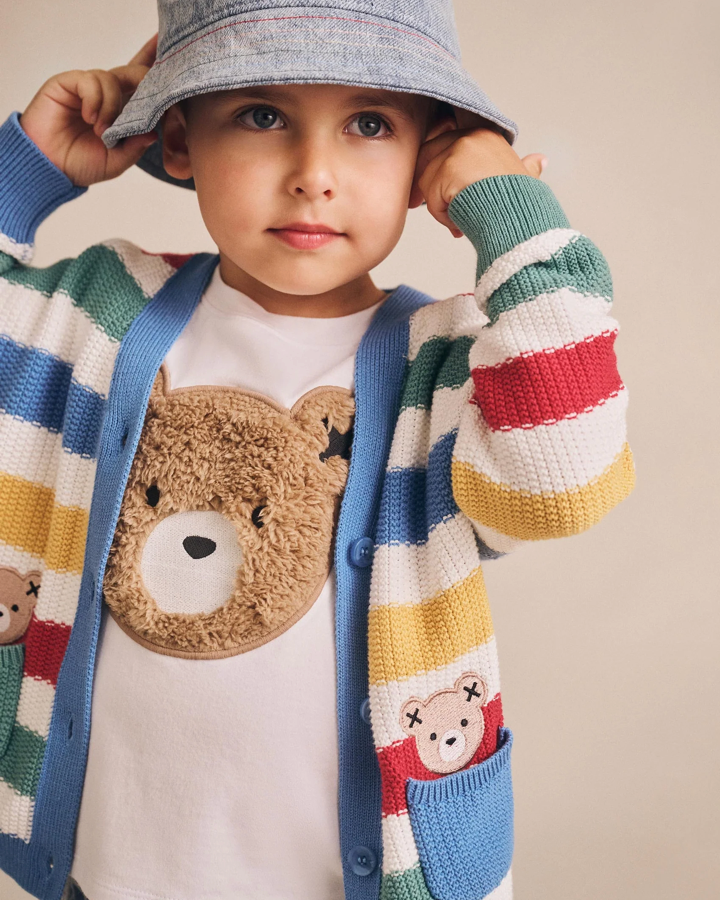 Child wearing a colorful striped sweater with bear designs and a gray bucket hat.