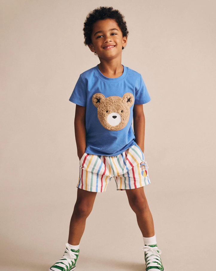 Child wearing a blue t-shirt with a bear design and colorful shorts on a beige background