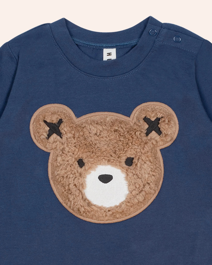 Navy blue shirt with a brown teddy bear face patch on a beige background