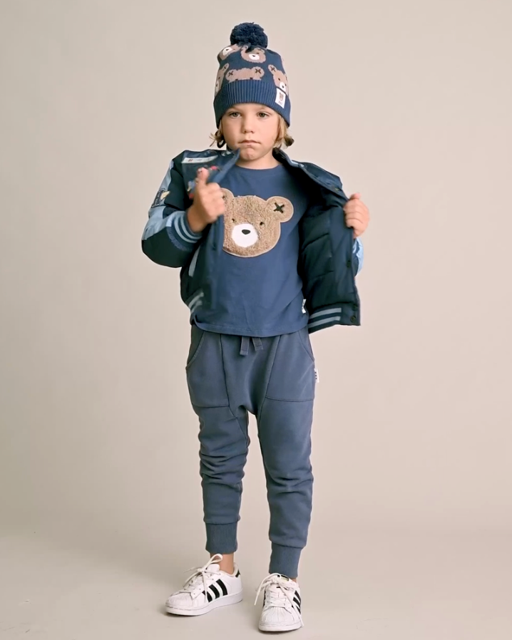 Child wearing a blue outfit with a bear design, standing against a plain background