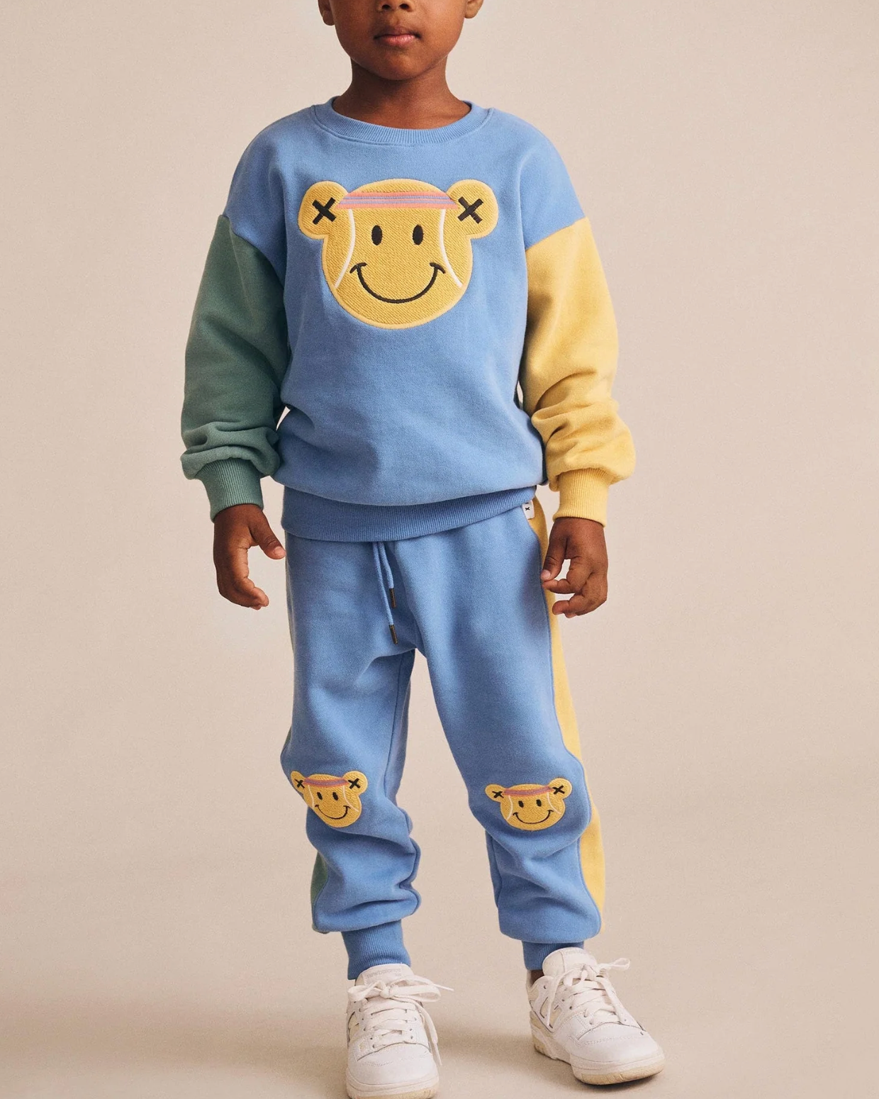 Child wearing a colorful outfit with a smiley face design on a beige background