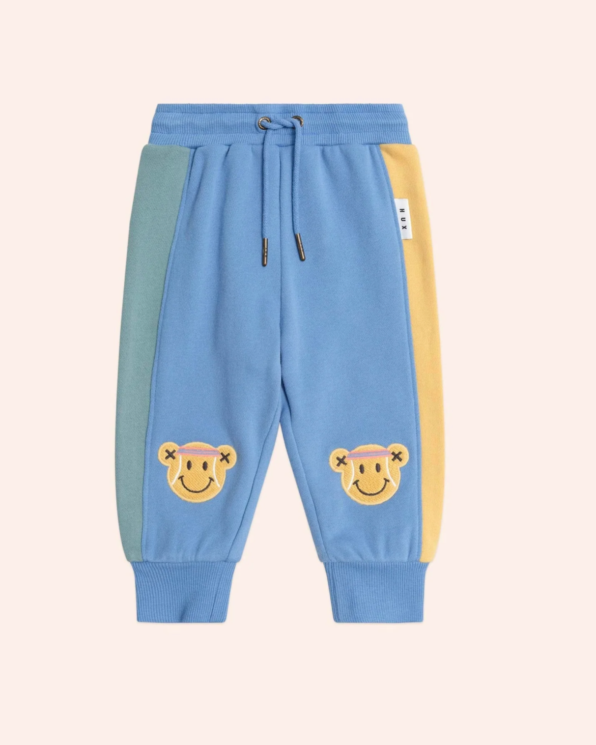 Blue jogger pants with smiley face designs on a light beige background