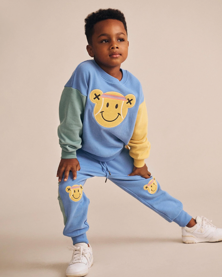 Child wearing a blue and yellow outfit with smiley face designs on a beige background