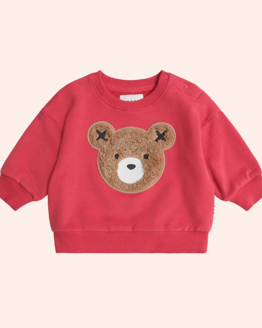 Red sweater with a teddy bear face patch on a light pink background