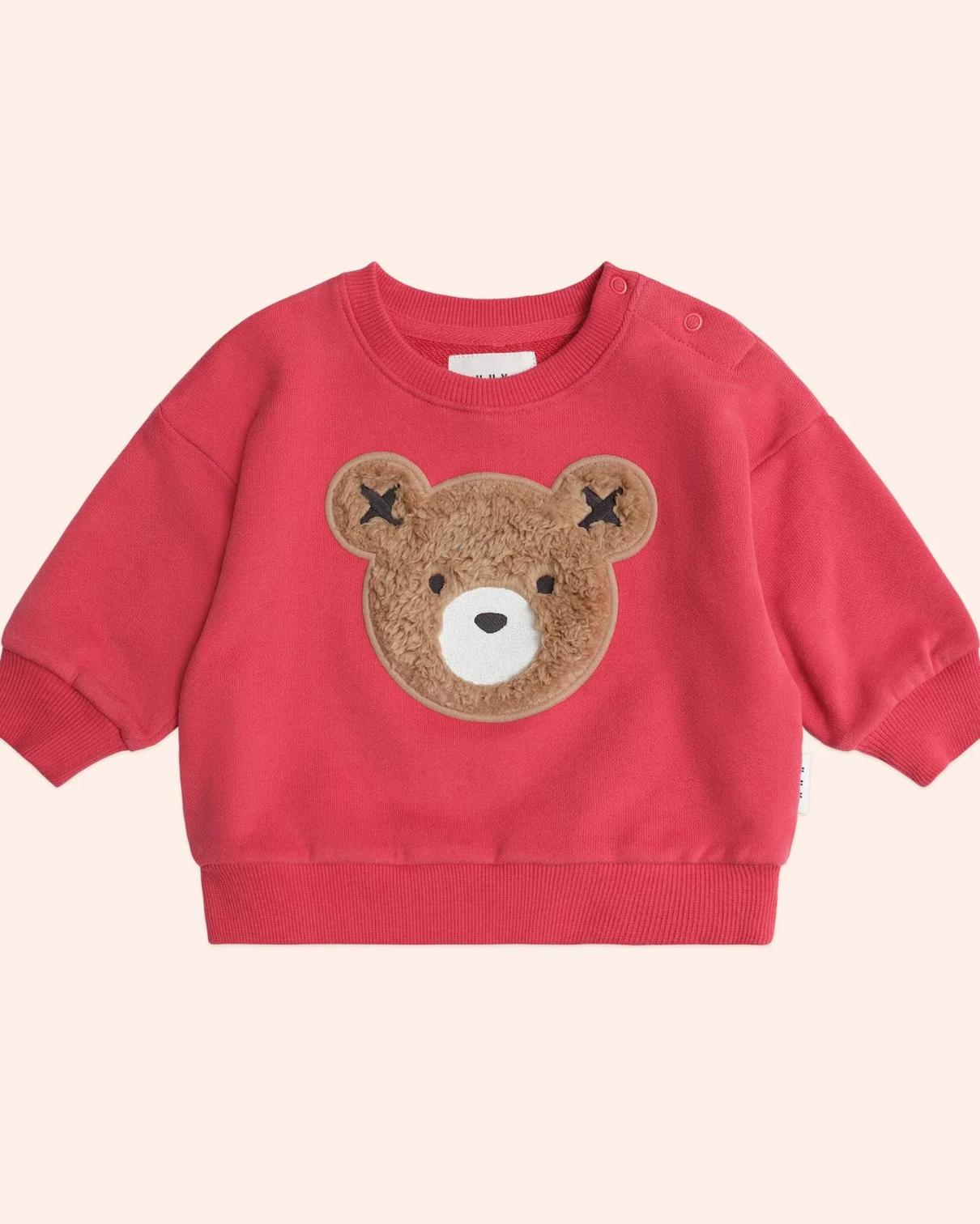 Red sweater with a teddy bear face patch on a light pink background