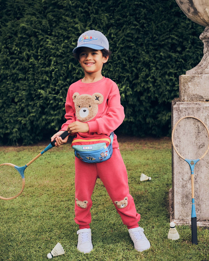 Child in pink outfit with bear design holding a badminton racket outdoors.