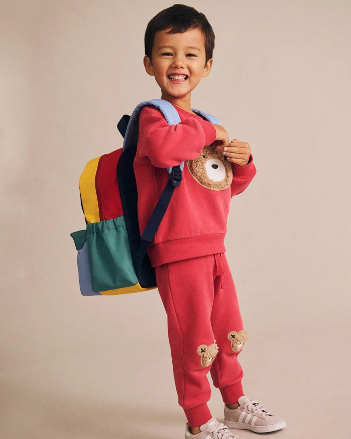 Child wearing a red outfit with a colorful backpack on a beige background