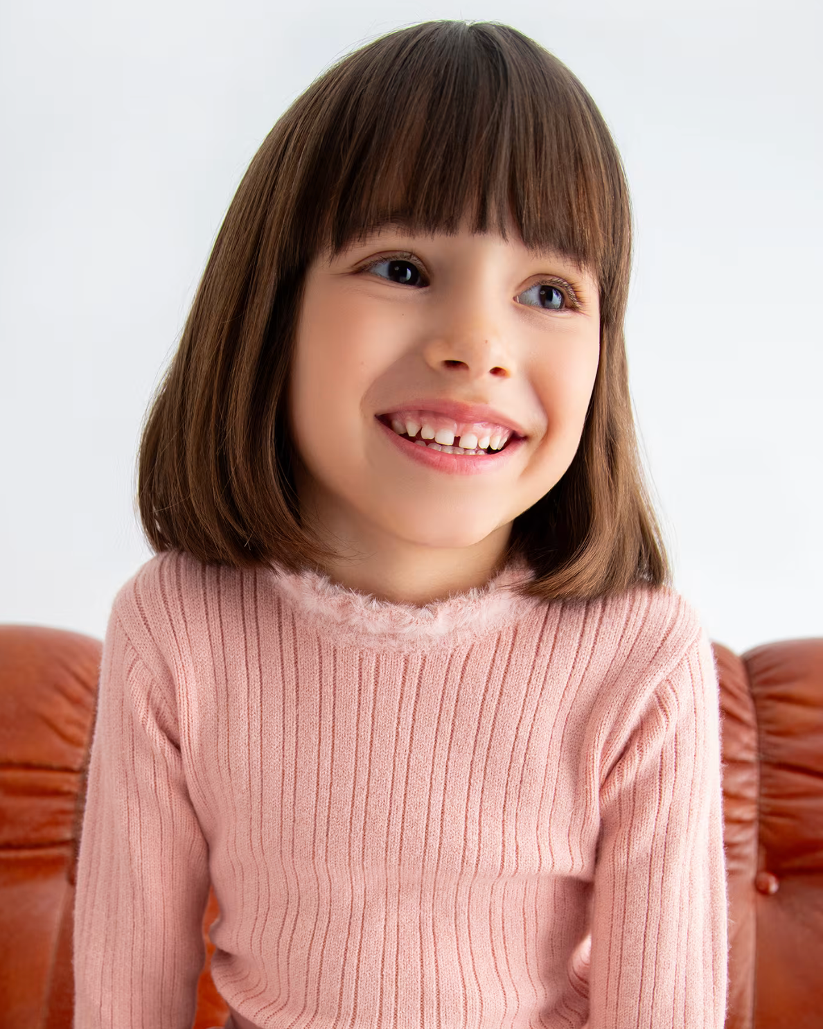 Young girl with a big smile wearing a pink sweater on a white background