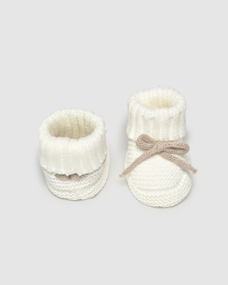 Pair of white baby booties with textured design on a light gray background