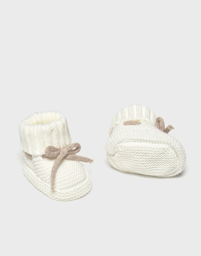 Pair of white knitted baby booties on a light gray background