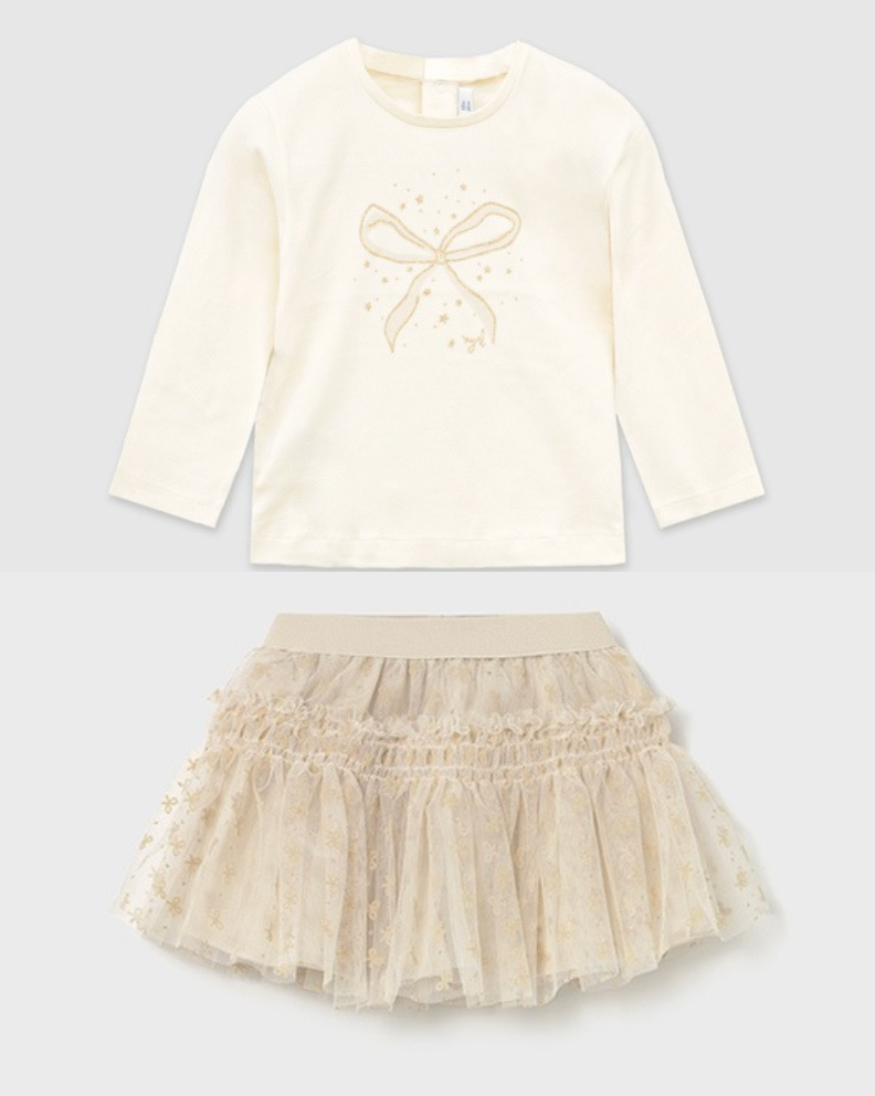 White long-sleeve top with bow design and beige skirt on a light gray background