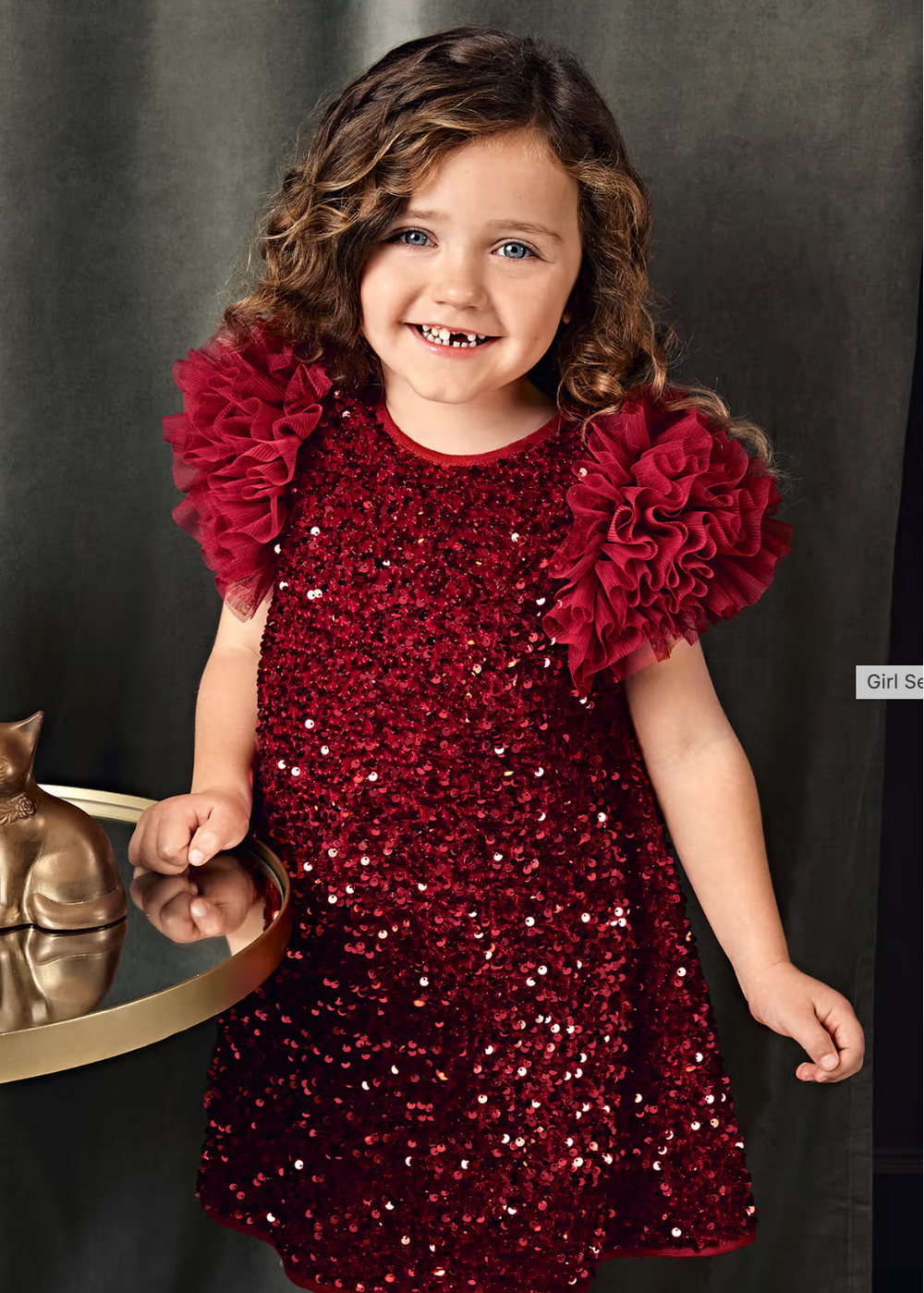 Young girl wearing a red sequin dress with ruffled sleeves against a dark background