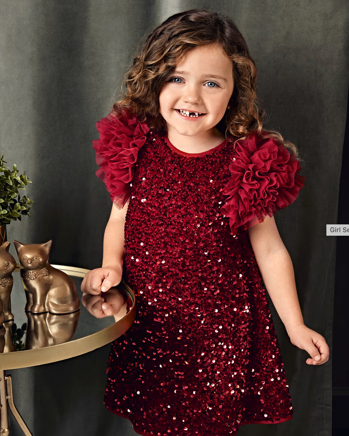 Young girl wearing a red sequin dress with ruffled sleeves against a dark background