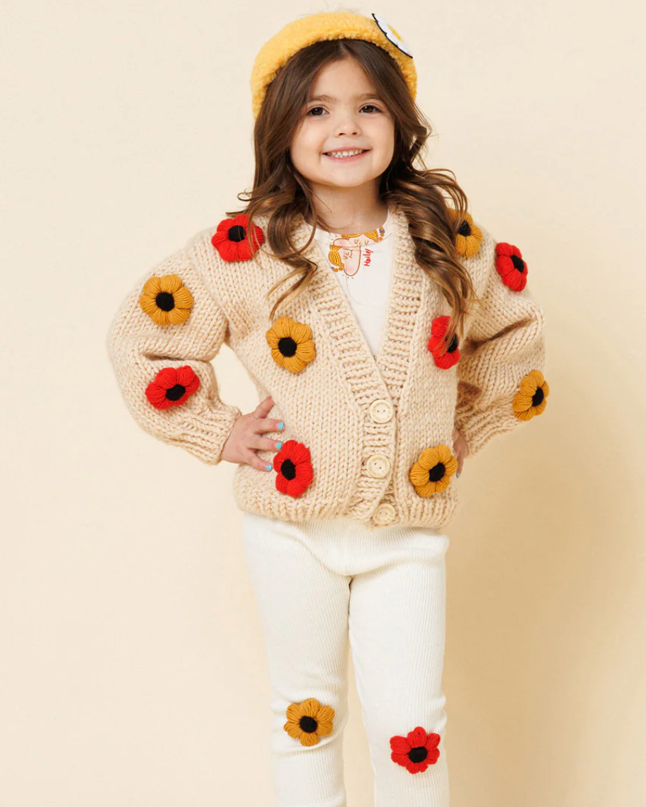 Child wearing a beige cardigan with flower patterns on a beige background