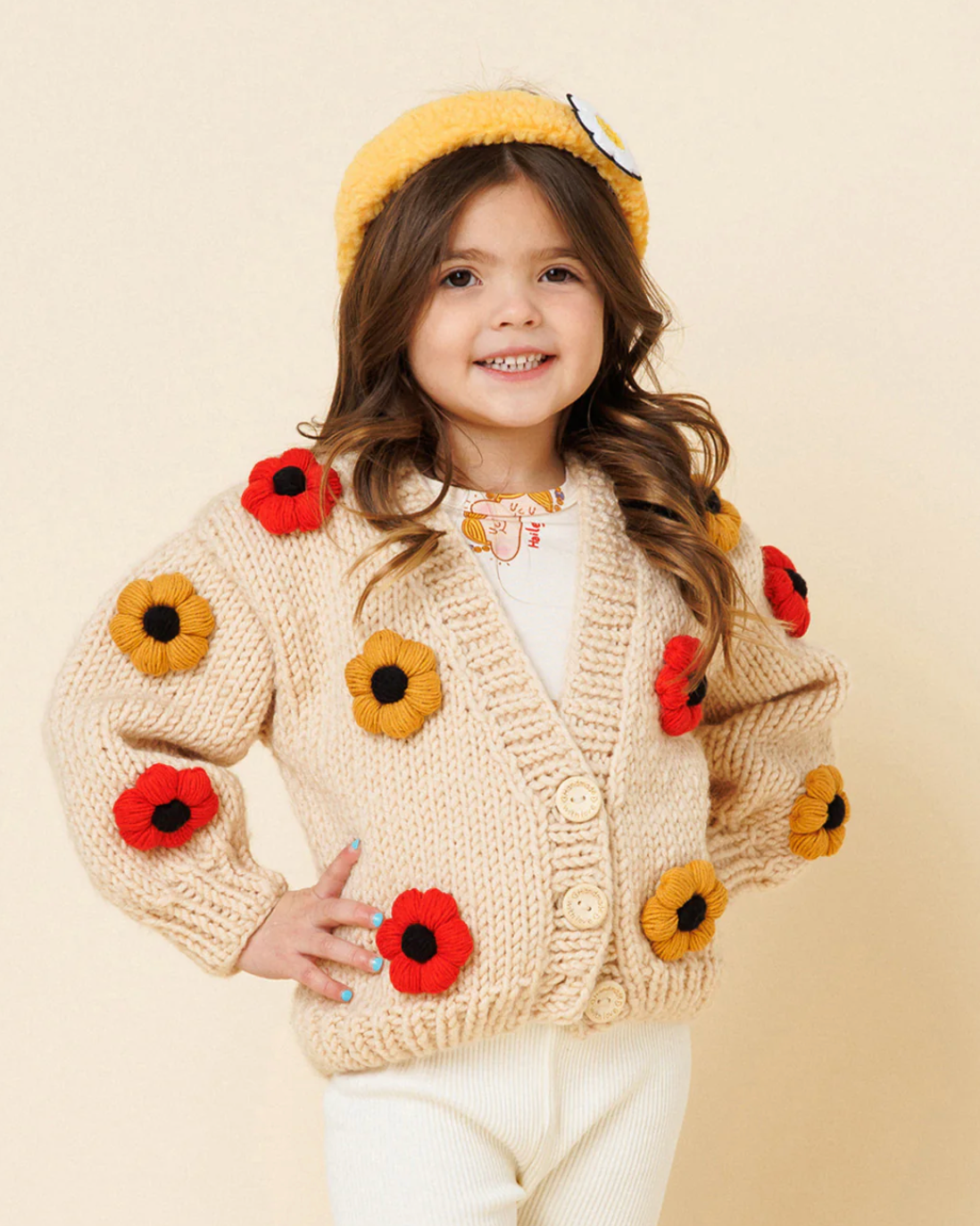 Child wearing a beige cardigan with flower patterns on a beige background