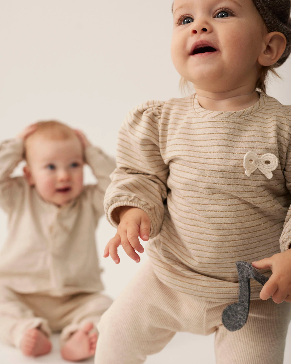 Two babies in beige outfits on a light background