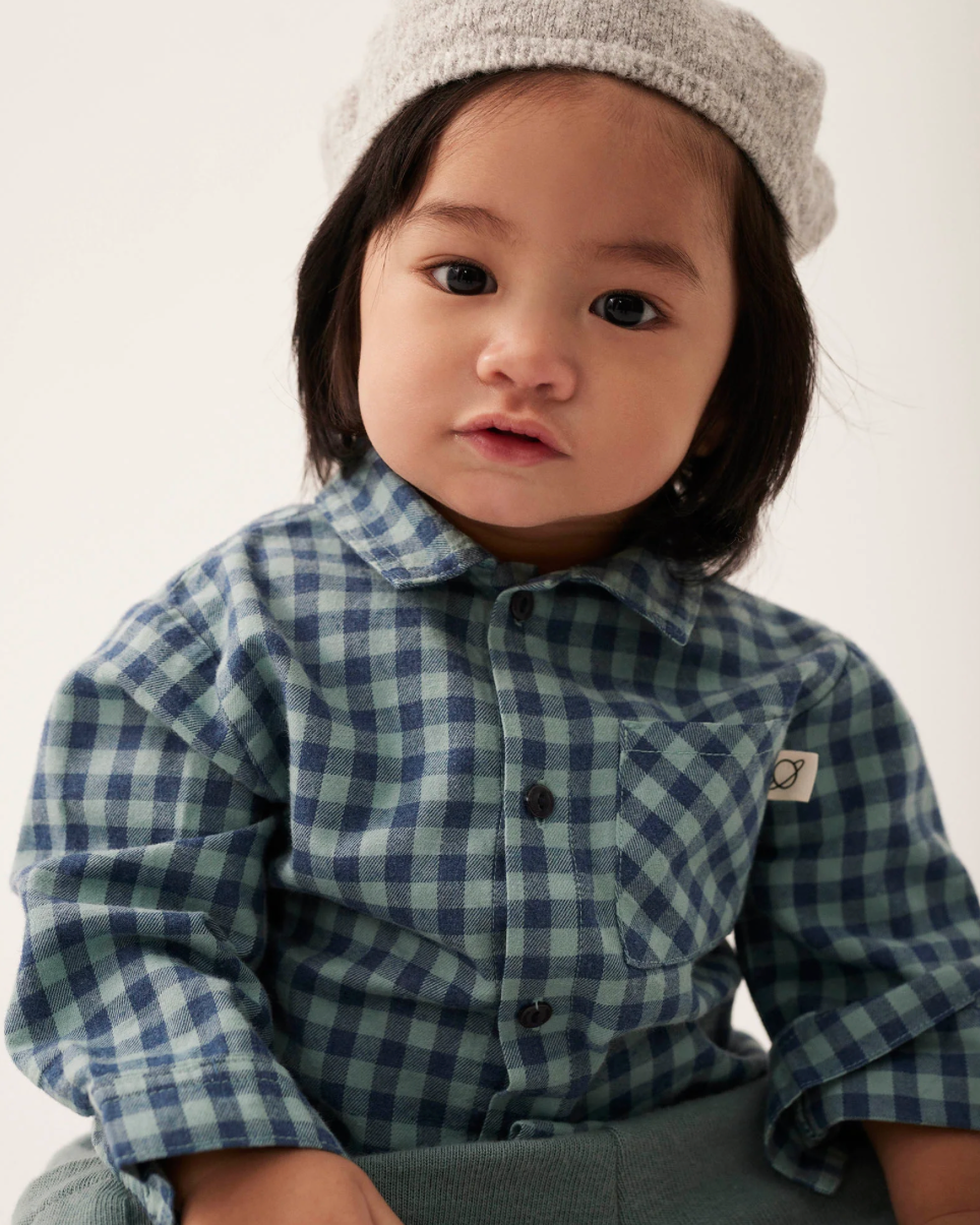 Child wearing a blue checkered shirt and gray pants with a white background
