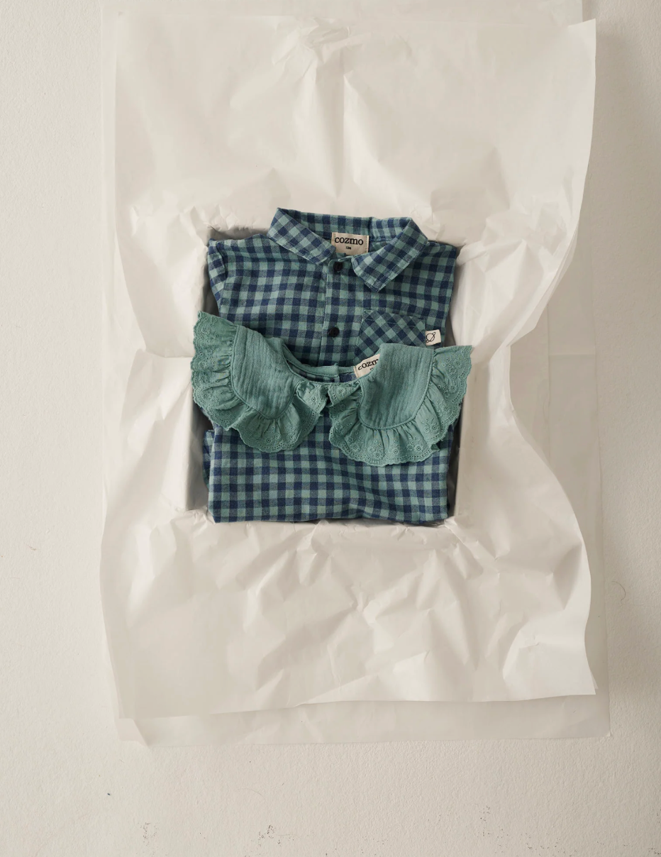 Green checkered shirt with ruffled details in a clear plastic bag on a light background