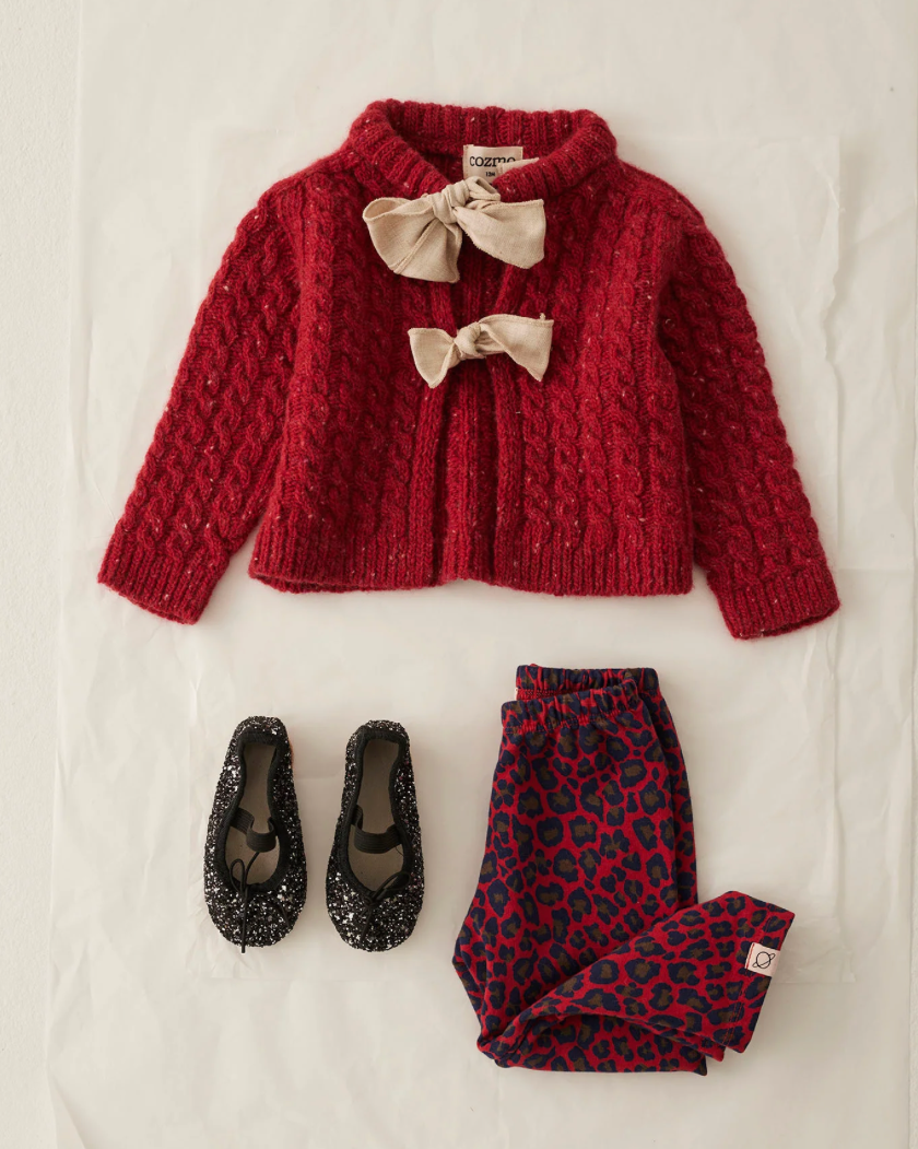 Red knitted cardigan with bow details, leopard print pants, and black sequin shoes on a light background
