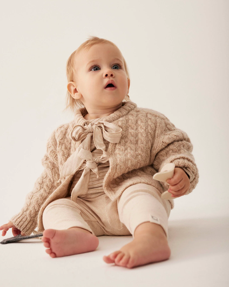 Baby wearing a beige knitted outfit on a white background