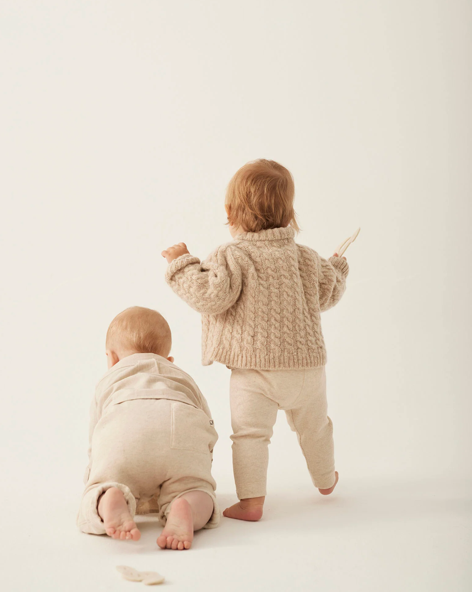 Two children in beige knitted outfits on a white background
