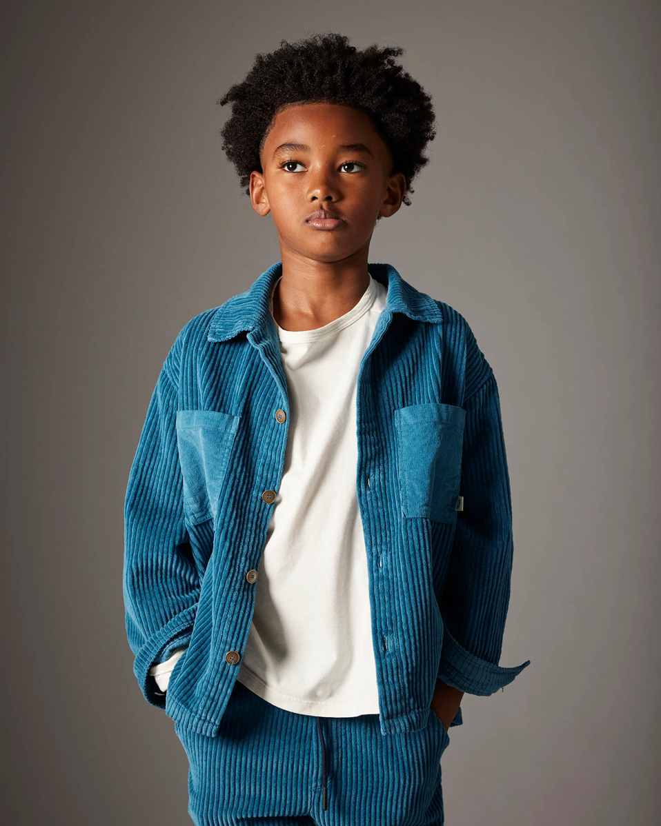 Child wearing a blue corduroy outfit against a gray background