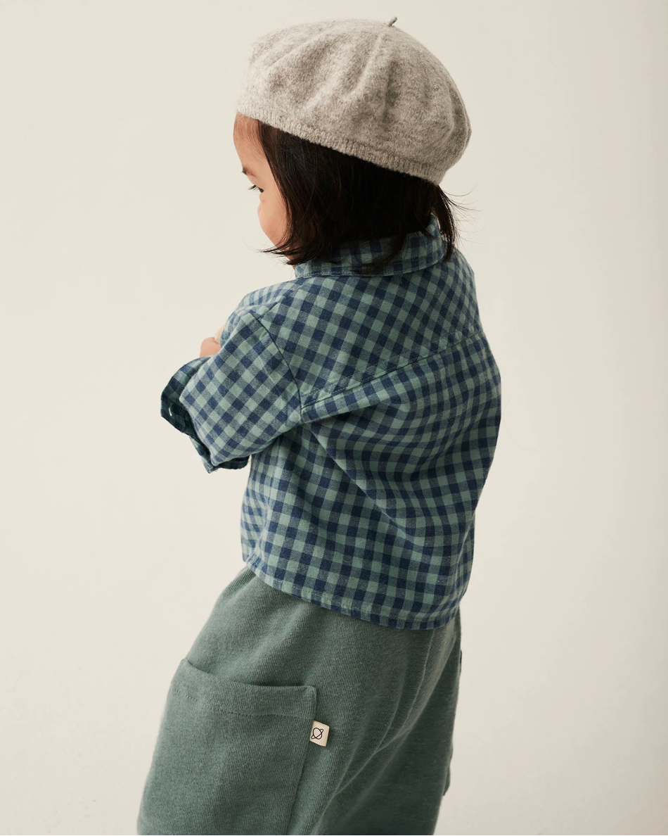 Child wearing a checkered shirt and beret against a plain background