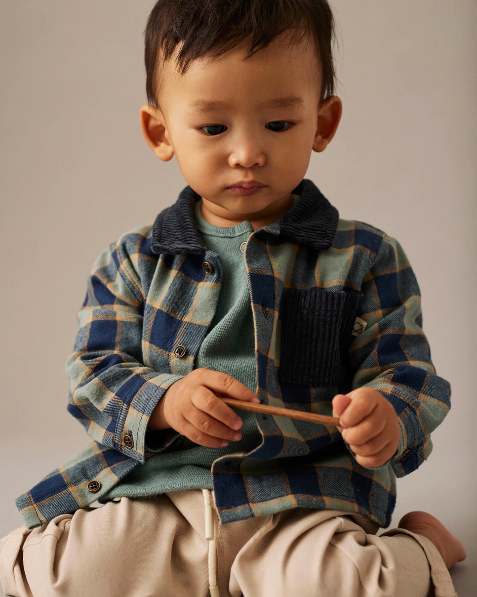 Child wearing a plaid shirt and holding a wooden object against a neutral background