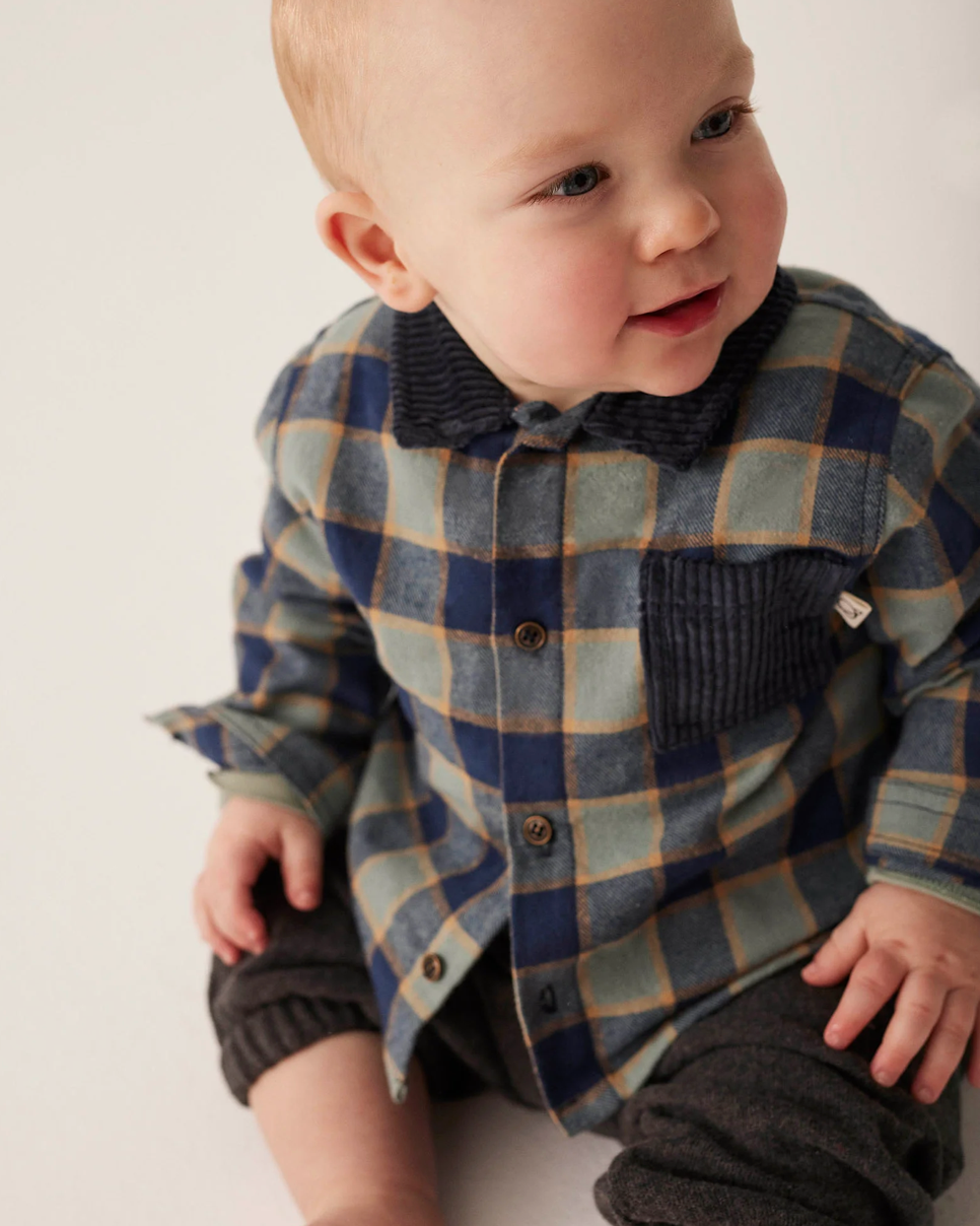 Baby wearing a plaid outfit on a plain background