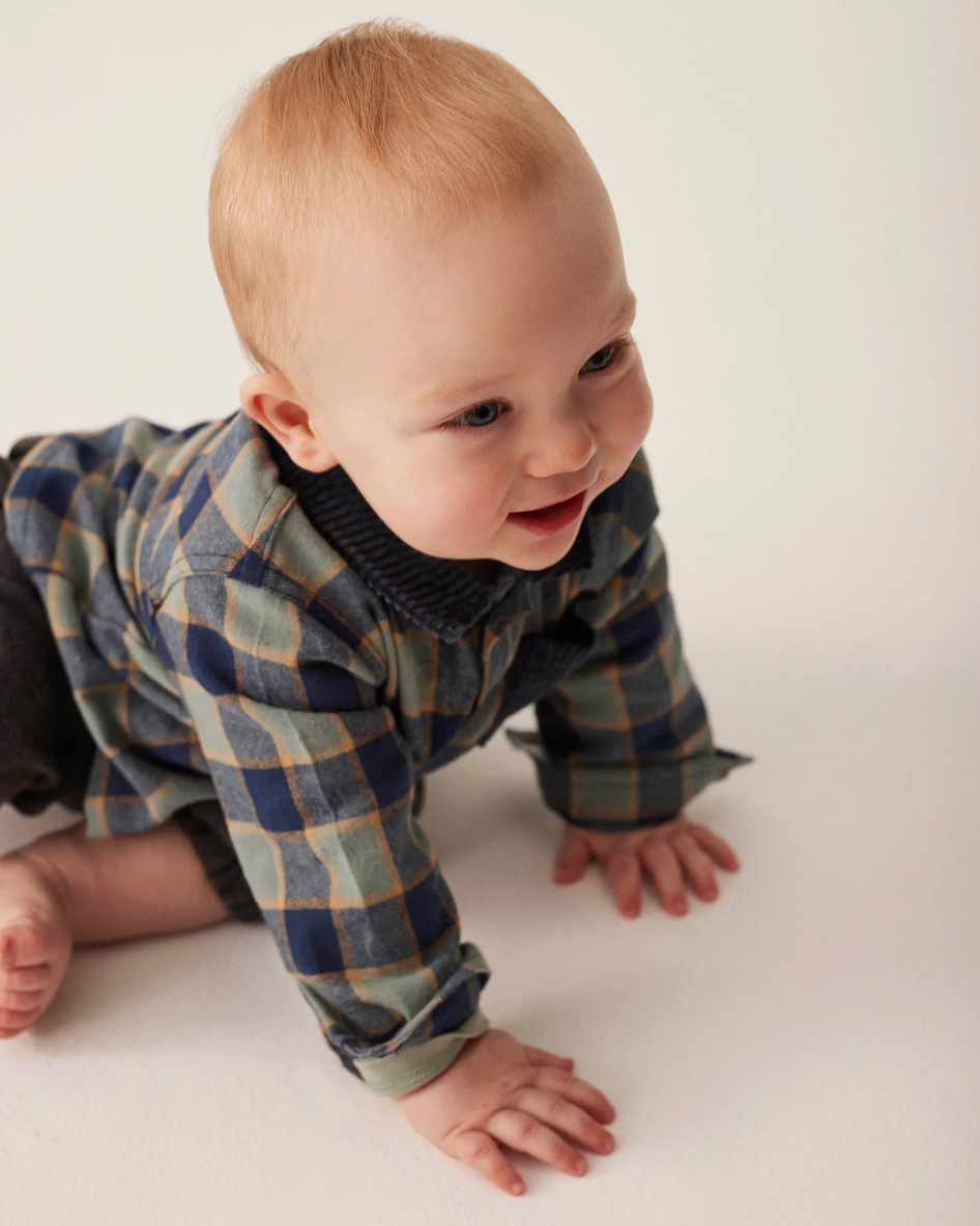 Baby in a plaid outfit crawling on a white surface