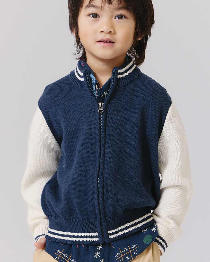 Child wearing a navy blue vest over a white shirt on a plain background