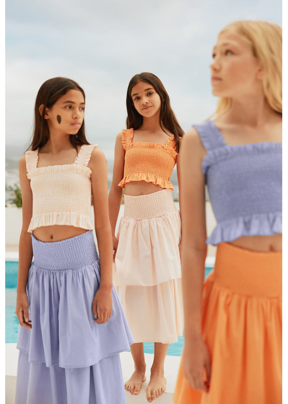 Three women wearing colorful outfits standing by a pool.