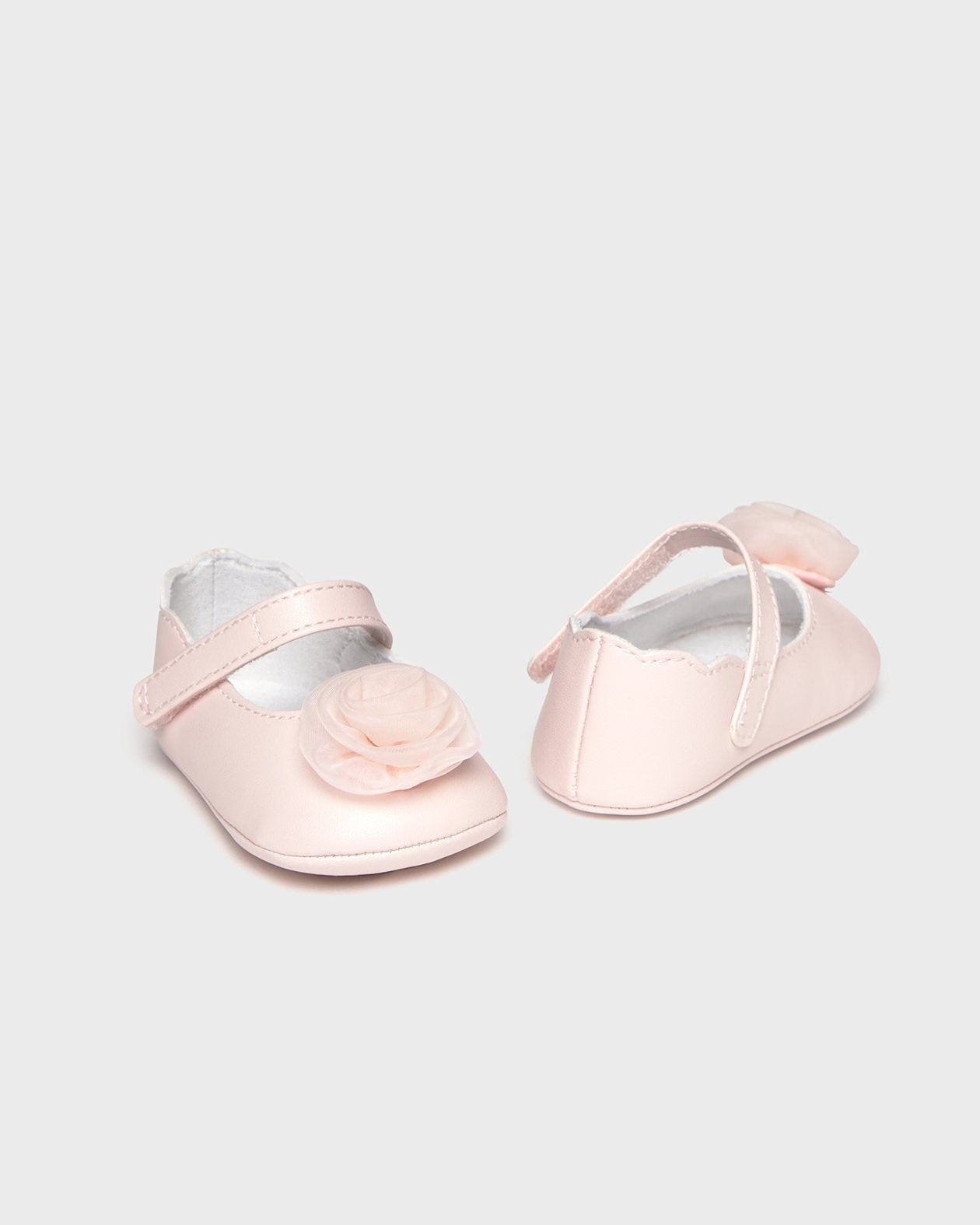 Pair of pink baby shoes with a bow on a light gray background