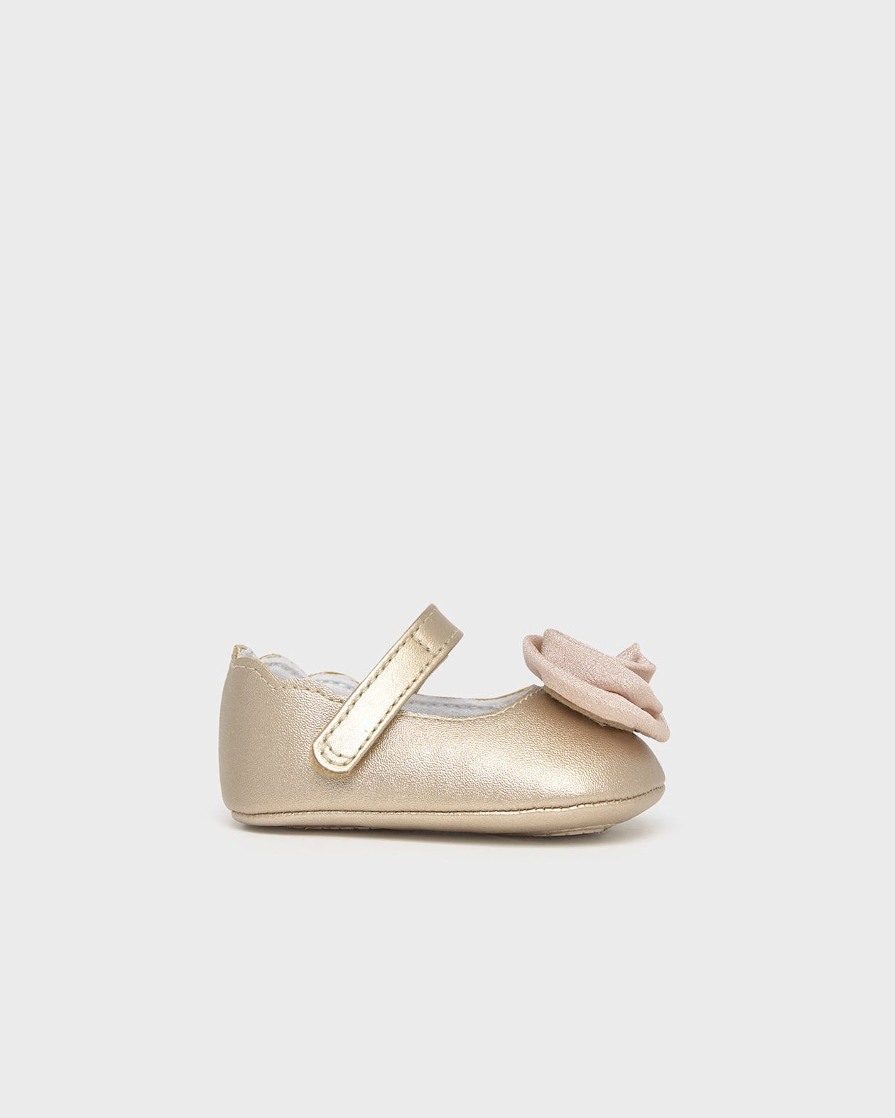 Gold baby shoes with a bow on a light gray background