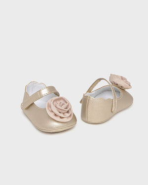 Pair of gold baby shoes with pink floral decorations on a light gray background