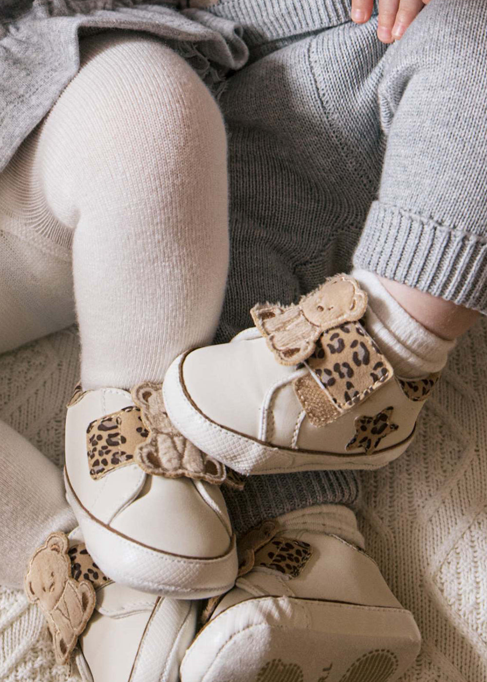 Children's white shoes with leopard print details worn by a child sitting on a textured surface.