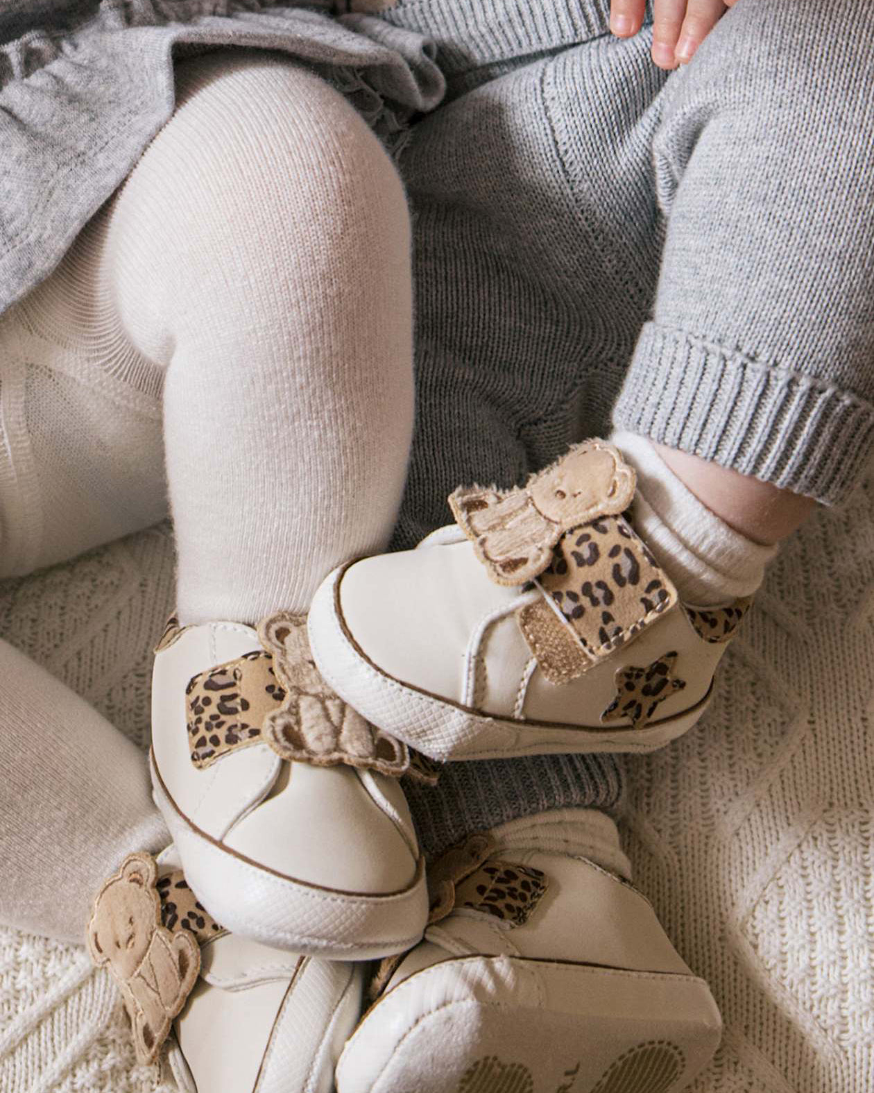 Children's white shoes with leopard print details worn by a child sitting on a textured surface.