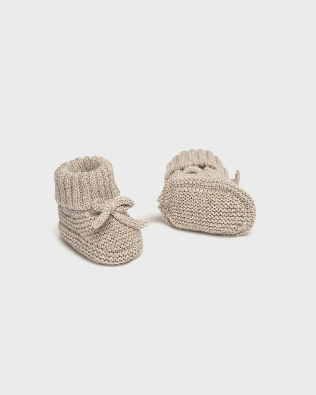 Pair of beige knitted baby booties on a white background